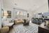 Chic modern living room with elegant decor, featuring a cozy tan sofa, artistic wall accents, and an open kitchen with stylish bar seating.