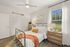 Charming bedroom with modern metal bed frame, bright white linens, and vibrant orange throw. Natural light floods through a large window, highlighting a cozy reading nook with a stylish wooden dresser and elegant decor.