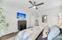 Bright and elegant bedroom with stylish decor, featuring a cozy bed, modern ceiling fan, and flat-screen TV displaying a tropical scene.