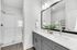 Modern bathroom with sleek double vanity, large mirror, and elegant glass shower, enhanced by tasteful decor and bright lighting.