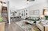 Elegant open-plan living space with a modern kitchen, cozy green sofa, and a chic coffee table. Natural light floods through large windows, highlighting contemporary decor and a stylish staircase.