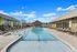 Luxurious apartment complex featuring a stunning outdoor pool with cozy lounge chairs and a modern poolside cabana under a bright blue sky.