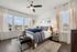 Elegant bedroom with large windows, natural light, and chic decor, featuring a cozy bed with blue accents and stylish furniture.