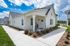 Charming white cottage with a modern porch and lush landscaping under a vibrant blue sky.
