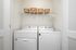 Modern laundry room featuring sleek white washer and dryer units with organized shelving and wicker storage baskets.