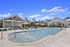 Luxurious outdoor pool area featuring lounge chairs, sun umbrellas, and a modern clubhouse under a bright blue sky.