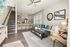 Bright and elegant living room with modern decor and open kitchen layout, featuring a cozy sofa, stylish artwork, and a staircase leading upstairs.