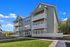 Modern three-story apartment building with spacious balconies and a striking green facade, set against a clear blue sky and lush greenery, offering serene living in a stylish environment.