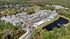 Stunning aerial view of a serene apartment community nestled between lush greenery and a tranquil lake, featuring modern buildings and a sparkling pool.