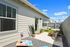 Charming outdoor patio with modern seating area, lush plants, and a playful cornhole game under a bright blue sky.
