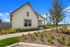 Charming single-story home with a pristine white exterior, lush landscaping, and a spacious front porch under a bright blue sky.