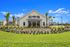 Charming clubhouse with a rustic design, surrounded by lush landscaping and vibrant flower beds under a clear blue sky.