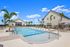 Luxurious outdoor pool area surrounded by palm trees and modern lounge chairs, with a stylish clubhouse in the background under a bright blue sky.