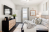 Elegant bedroom with modern decor, featuring a cozy bed, stylish dresser, and a mounted flat-screen TV, illuminated by natural light through large windows.