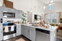 Modern open kitchen with sleek gray cabinetry, stainless steel appliances, and elegant pendant lighting, seamlessly connected to a bright, stylish living area.