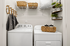 Chic laundry room with modern washer and dryer, elegant woven baskets, and stylish shelving for a tidy and functional space.
