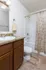 A small, tidy bathroom with a granite countertop, wooden cabinets, sink, and a towel hanging. The shower has a floral curtain, creating a cozy atmosphere.