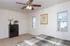A neatly furnished bedroom with a checkered bedspread, dark dresser, ceiling fan, two windows with blinds, and framed artwork on a white wall.