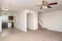 Unfurnished living room with beige carpet, white walls, a ceiling fan, and a glimpse of a kitchen. Stairs lead to a second floor, creating an open, airy feel.