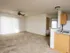 Unfurnished living space with neutral carpet, ceiling fan, and open layout leading to kitchen and hallway.