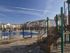 Playground with slides in the foreground, adjacent to a fenced pool surrounded by multi-story apartment buildings under a clear blue sky.
