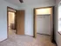 Interior view of a bedroom with carpeted flooring, featuring an open closet with bi-fold doors on the right and an open door leading to a bathroom on the left. Natural light filters through a nearby window, giving the room a soft, warm feel.