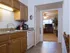 View from the kitchen into the living room, showing wood cabinetry, white appliances, and tile flooring transitioning into carpeted space.