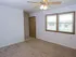 Empty bedroom with beige carpet, white walls, a ceiling fan, double window, and small walk-in area near a wooden door.