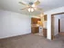 View of an open dining and kitchen area with carpeted floors, ceiling fan, and compact kitchen with wood cabinetry and white appliances.