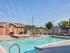 Sunny outdoor swimming pool with hot tub, brick clubhouse, and lounge seating at Embassy Ozark Apartments.