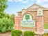 Sign for Willow Creek Apartments, featuring a tree logo and surrounded by greenery and brick architecture under a clear blue sky.
