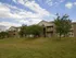 Modern apartment building with large windows, surrounded by green lawn and trees under a partly cloudy sky.