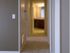 A beige-carpeted hallway with soft lighting leads to a warmly lit bathroom at the end. Wooden cabinets and a large mirror are visible in the distance.