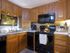 Cozy kitchen with wooden cabinets, black appliances including stove and microwave. A coffee maker and mixer on counter, towel on oven handle.