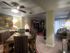 Cozy living and dining area with warm lighting. Includes a wooden dining table, chairs with patterned upholstery, a TV console, and a couch by sliding doors.