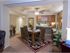 Elegant dining room with a wooden table, cushioned chairs, and a floral rug. Warm lighting, ceiling fan, and decorative plants create a cozy, inviting atmosphere.