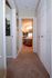 A carpeted hallway leads to a well-lit bathroom with a red rug and wooden cabinets. Walls are adorned with framed pictures, giving a cozy, inviting feel.