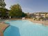 Outdoor swimming pool in a sunny courtyard, surrounded by trees and buildings. Lounge chairs and a life preserver are visible, creating a relaxed atmosphere.