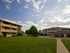 A sunny courtyard between two apartment buildings, featuring a neatly trimmed lawn and scattered clouds in the blue sky, conveys a serene atmosphere.