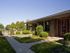 Single-story home with brick facade, red door, and manicured landscaping featuring bushes and trees. Clear blue sky in the background, creating a tranquil atmosphere.