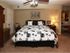 Cozy bedroom with a king-sized bed adorned with a black-and-white patterned comforter. A lit lamp and artwork frame the warm, inviting atmosphere.