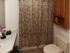 Small bathroom with floral patterned shower curtain, beige tiles, wooden cabinets, and a white countertop. A small plant adds a touch of greenery. Cozy and clean.