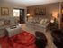 Cozy living room with beige sofas, colorful pillows, warm lighting, a vibrant red rug, and sliding glass doors leading to a balcony. Peaceful ambiance.