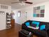 Cozy living space with hardwood floors, dark sofa, bright blue accent pillows, ceiling fan, and colorful wall art&mdash;stylishly decorated for comfort.