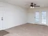A spacious living room with soft beige carpeting and a ceiling fan with a light fixture. White French doors with blinds built inside the glass panels lead to an outdoor area. The walls are painted in a neutral off-white tone.
