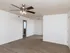 Spacious living room with light wood-look vinyl flooring, white walls, and a ceiling fan with light fixture. The room has an open layout, leading to a hallway and the kitchen area.