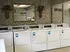 Laundry room with multiple white dryers, decorative wallpaper, wall art, and a large mirror at English Village.