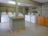 Spacious laundry room with multiple machines, central folding table, and utility counter at English Village.