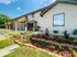 Front of leasing office with bright landscaping, stone-bordered flower beds, and visible apartment entrances.