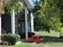 Apartment exterior with brick and siding, featuring a balcony. A red picnic table sits beneath a tree on a grassy lawn, creating a peaceful setting.